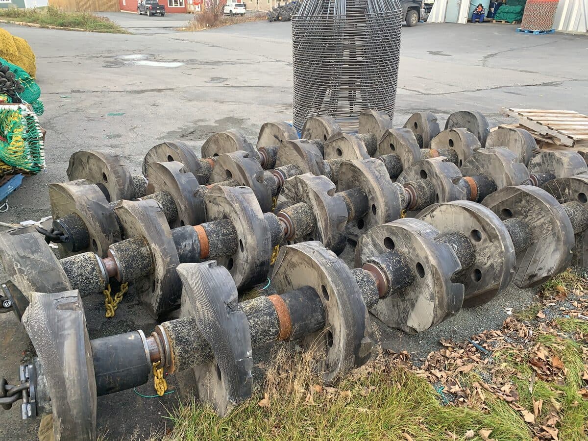 Rows of rubber disc groundgear threaded on wire and laid out on the yard, net drums stacked behind.