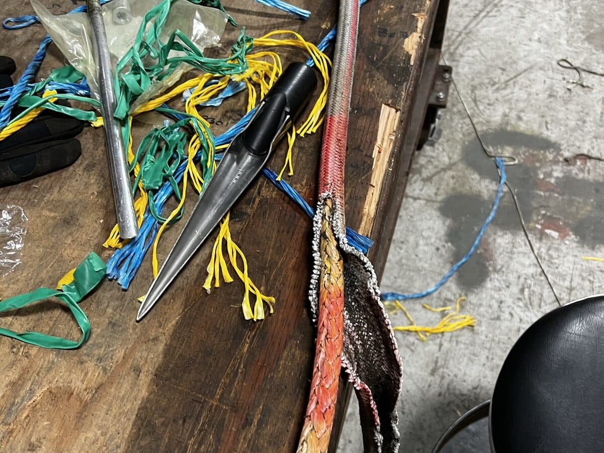 A splicing bench with steel fids, coloured twine offcuts and a rope with its cover opened back for a tuck.
