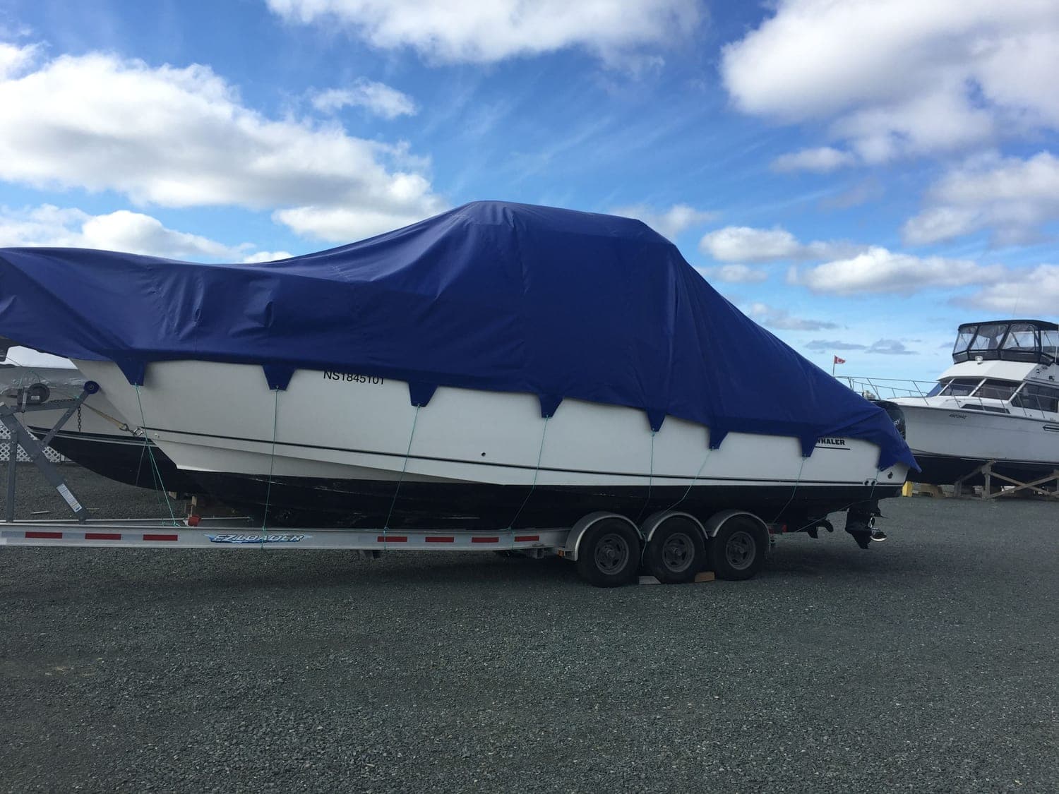 A boat on its trailer under a fitted navy cover drawn down over the gunwales